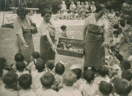 École de Plein-Air, distribution du goûter aux enfants assis en extérieur : photographie noir et blanc.