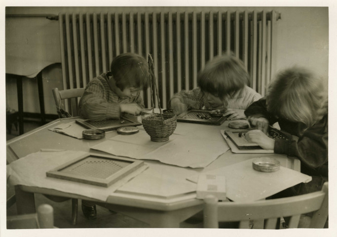École maternelle de la route des Petits-Ponts, enfants assis autour d'une table dans une salle de classe : photographie noir et blanc.