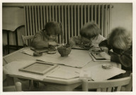 École maternelle de la route des Petits-Ponts, enfants assis autour d'une table dans une salle de classe : photographie noir et blanc.