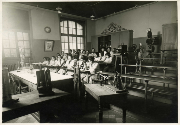 Centre d'apprentissage de l'école Sadi-Carnot, mise en scène dans une salle de classe représentant un cours de biologie dispensé à des jeunes filles : photographie noir et blanc.