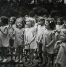 École de Plein-Air, groupe d'enfants chantant debout sur des chaises en extérieur : photographie noir et blanc.