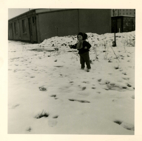 Portrait de Josiane Pillot devant un bâtiment de la cité d'urgence des Courtillières : photographie en noir et blanc.