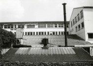 Usine Motobécane désaffectée, vue de l'extérieur sur les toitures et une partie des bâtiments : photographie noir et blanc.
