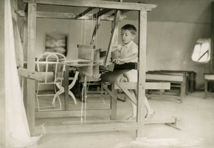 École de Plein-Air, enfant faisant du tissage sous une tente : photographie noir et blanc.