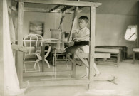 École de Plein-Air, enfant faisant du tissage sous une tente : photographie noir et blanc.