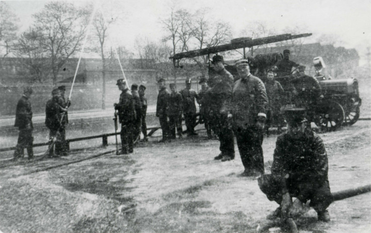 Pompiers avec un véhicule motorisé au bord du canal : reproduction de photographie noir et blanc.