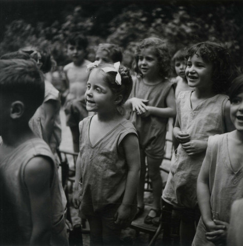 École de Plein-Air, groupe d'enfants chantant debout sur des chaises en extérieur : photographie noir et blanc.