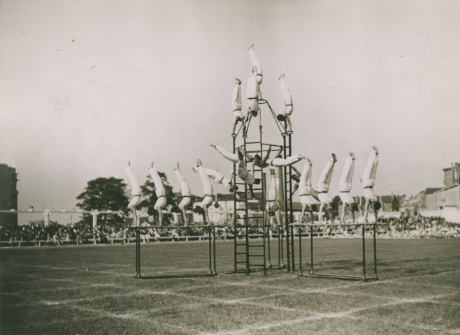 Fête d'éducation physique, démonstration d'équilibre sur des barres parallèles et sur une structure en hauteur : photographie noir et blanc.