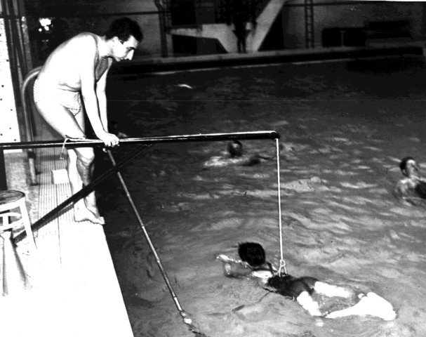Portrait de Jean Taris, champion de natation médaillé aux Jeux olympiques de Los Angeles de 1932 et premier directeur de la piscine municipale, apprenant à nager à un enfant : photographie noir et blanc.