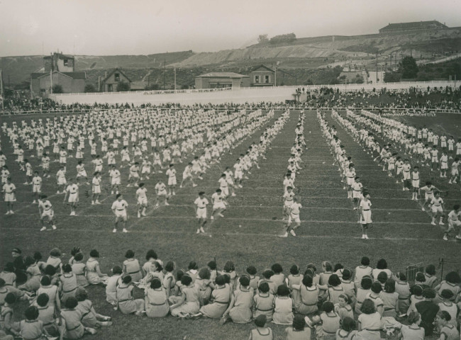 Fête d'éducation physique, vue large sur les mouvements d'ensemble, les spectateurs et les alentours à l'est du stade : photographie noir et blanc.