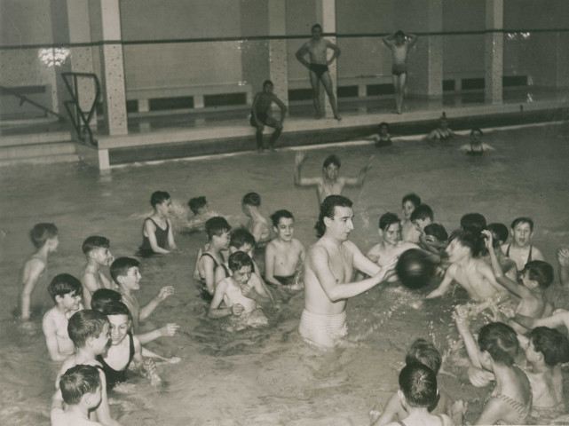 Piscine municipale, enfants jouant au ballon dans l'eau avec Jean Taris : photographie noir et blanc.