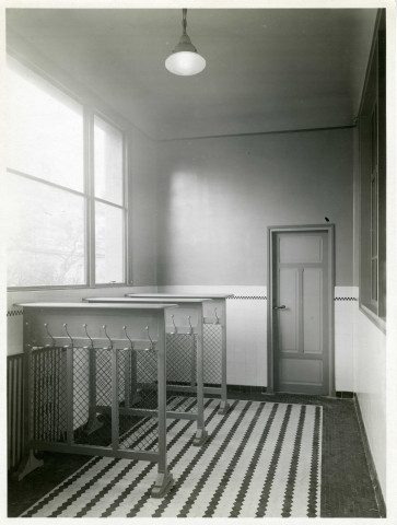 École maternelle de la route des Petits-Ponts, porte-manteaux dans un couloir de l'établissement scolaire : photographie noir et blanc.