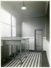 École maternelle de la route des Petits-Ponts, porte-manteaux dans un couloir de l'établissement scolaire : photographie noir et blanc.